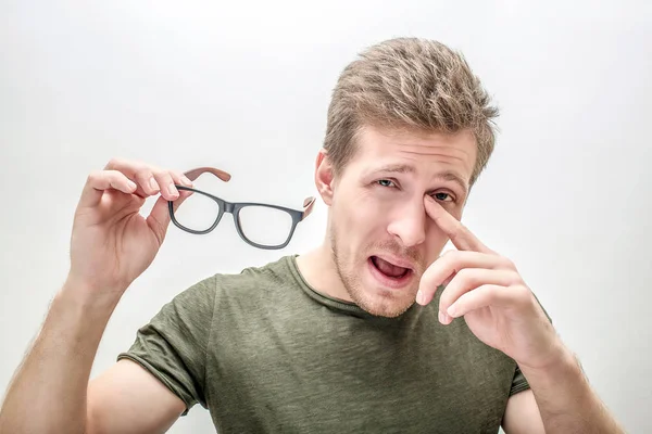 Young man stand and hold glasses in hand. He points on eyes and nose. Guy has bad sight. Isolated on white background. — Stock Photo, Image