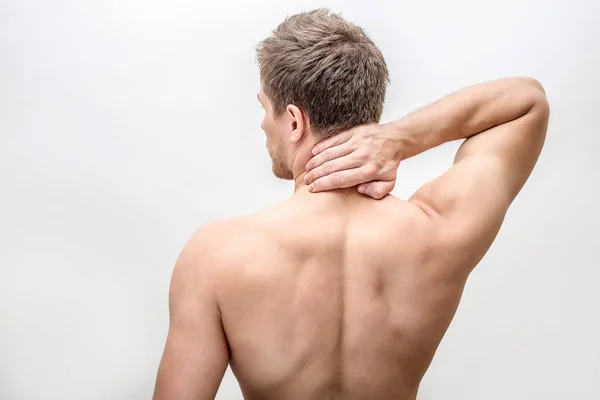 Un joven sin camisa se pone de pie y coge la mano del cuello. Siente dolor allí. El tipo muestra su espalda. Aislado sobre fondo blanco . — Foto de Stock