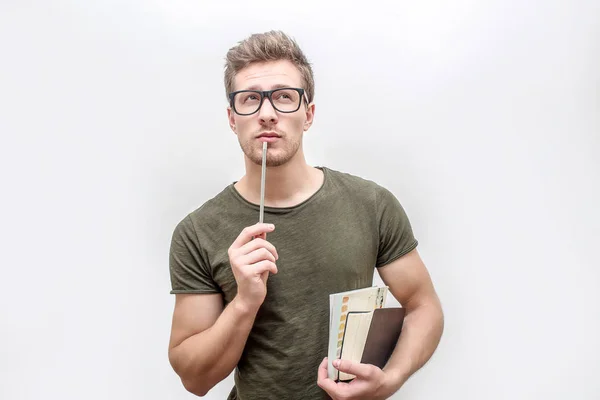 Young man in green shirt hold books and pencil in hands. He looks on camera through glasses. Isolated on white background. — Stock Photo, Image