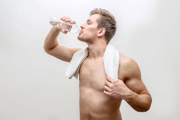 Sida skott av ung välbyggd man dricksvatten. Han håller vit handduk runt halsen. Isolerad på vit bakgrund. — Stockfoto