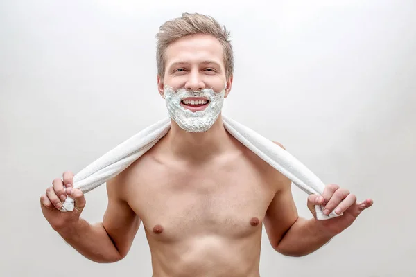 Happy young man with foam on beard look straight. He hold towel in hands behind neck. Guy smiling. Isolated on white background.