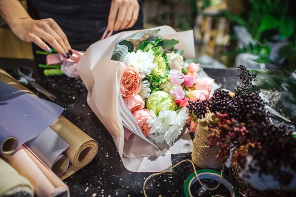 Primer plano de hermosa bouqette de flores que yacen sobre la mesa. Hay rollos de papel y flores. Ramo de tacto de mujer con manos . — Foto de Stock