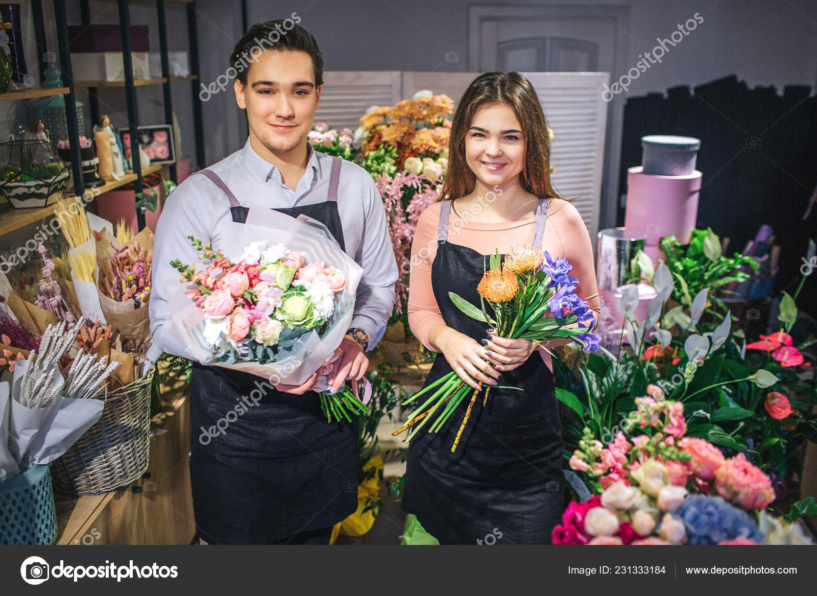 两个花商站着看镜头的照片 他们拿着花束 微笑着 销售人员很开朗 他们站在满屋子的花和植物里 图库照片 C Estradaanton