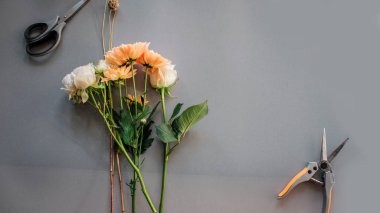 Beyaz güller ve turuncu papatya birlikte gri arka plan üzerinde bir buket yalan. Orada makas ve kerpetenler.