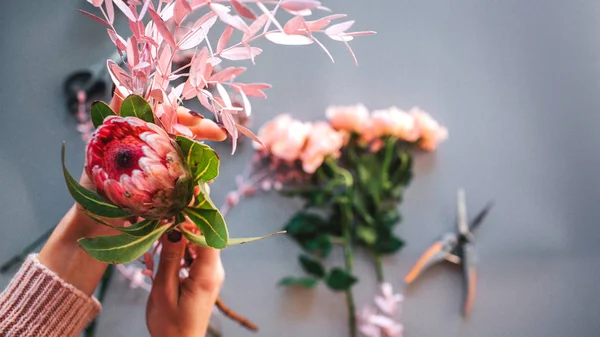Las manos de las mujeres sostienen hermosa flor roja y fronda. Rosas acostadas junto con alicates. Aislado sobre fondo gris . — Foto de Stock