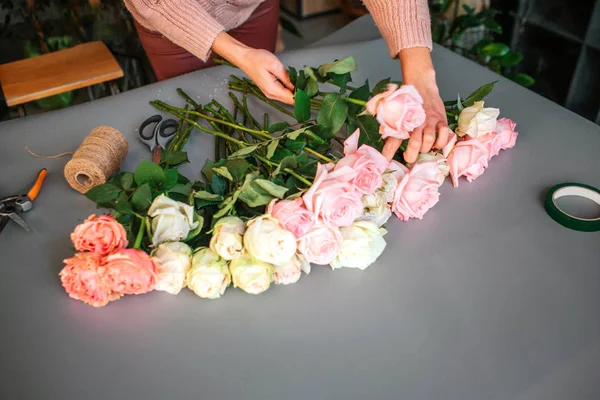 Foto de las manos de las mujeres poniendo rosas juntas en la mesa gris. Hilo de bobina acostado allí con pinzas y tijeras . — Foto de Stock