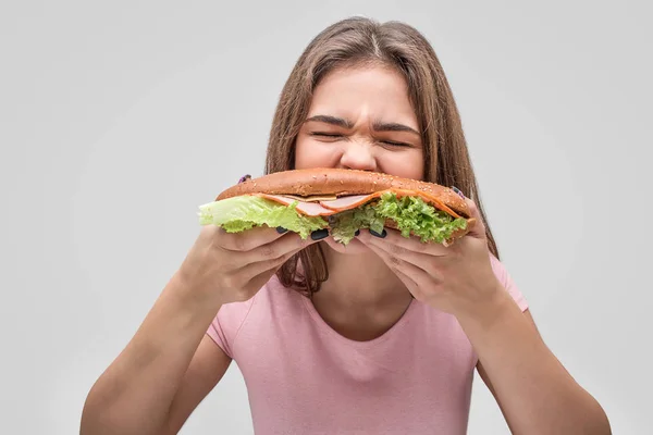 Hambre mujer joven muerde hamburguesa. Ella lo devora. Aislado sobre fondo gris . — Foto de Stock