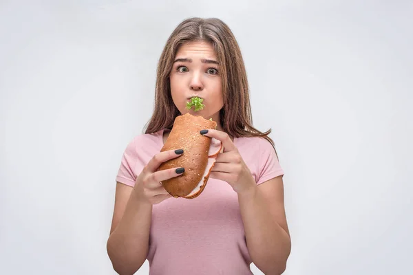 Jonge vrouw houd stuk groene sla in mond afgevraagd. Ze houden van de hamburger en kijk op de camera. Geïsoleerd op een grijze achtergrond. — Stockfoto
