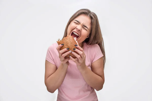 Happy young woman hold burger. She is going to eat it. Model is emotional. Isolated on grey background. — Stock Photo, Image