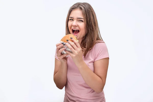 Gelukkig jonge vrouw kijken op camera met mond geopend. Ze houden de hamburger met beide handen. Geïsoleerd op witte achtergrond. — Stockfoto