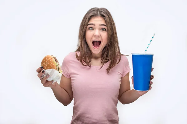 Gelukkig jonge vrouw schreeuwen op de camera. Ze hamburger en kopje cola in handen houden. Geïsoleerd op witte achtergrond. — Stockfoto
