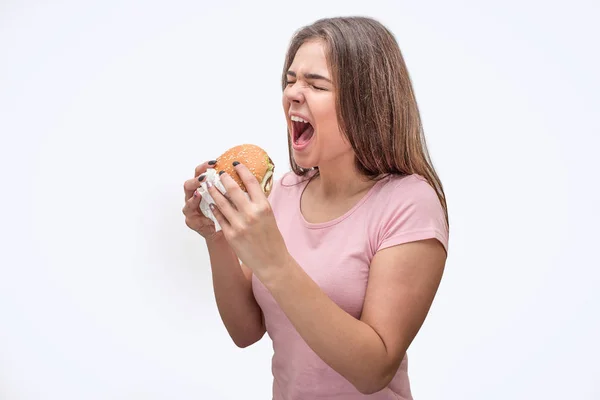 Jonge vrouwen houden mond geopend. Ze hamburger in handen houden. Model gaat eten. Geïsoleerd op een grijze achtergrond. — Stockfoto