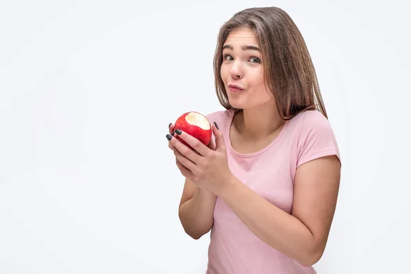 Bella e attraente giovane donna guarda sulla macchina fotografica e tenere mela morsa. Lei è sorpresa. Isolato su sfondo bianco . — Foto Stock