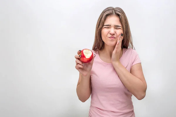 Несчастная молодая женщина держится за щеку. У нее болят зубы. Модель страдает. У неё яблоко под рукой. Изолированный на сером фоне . — стоковое фото