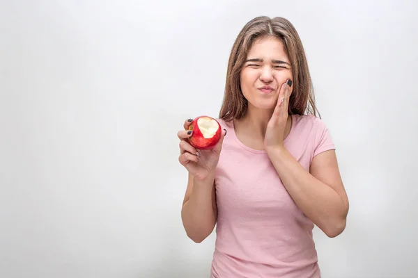 stock image Unhappy young woman hold hand on cheek. She has toothache. Model suffer. She has apple in hand. Isolated on grey background.