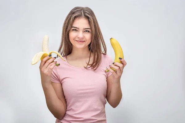 Веселая молодая женщина смотрит в камеру. Она держит в руках два открытых банана. Изолированный на белом фоне . — стоковое фото