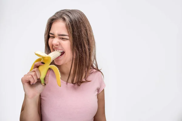 Walging jonge vrouw krimpen tijdens het bijten stukje banaan. Geïsoleerd op witte achtergrond. — Stockfoto