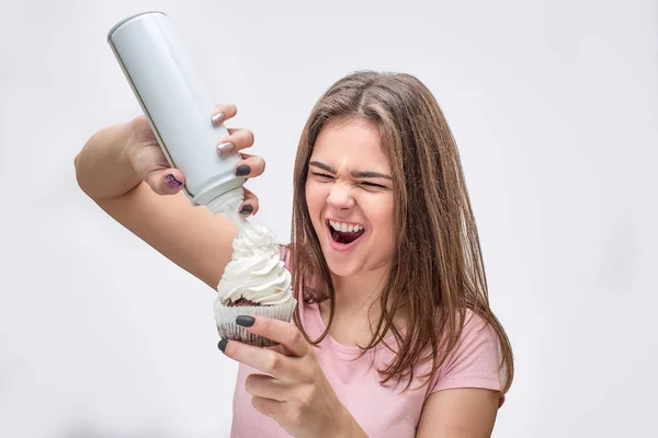 Grappige jonge vrouw zet wat room op de taart. Ze verschrompelen wonder. Geïsoleerd op een grijze achtergrond. — Stockfoto