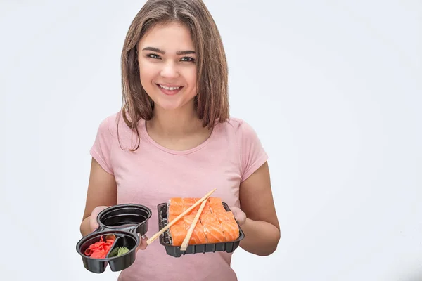 Позитивна молода жінка тримає соєвий соус з імбиром і суші в руках. Модель дивиться на камеру. Ізольовані на білому тлі . — стокове фото