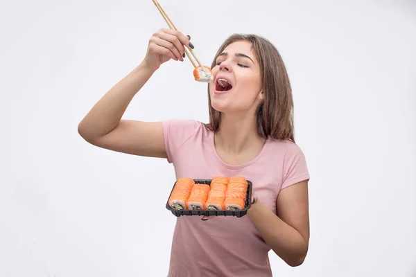 Vrolijke jonge vrouw leg stuk roll in mond. Ze gebruiken shopsticks. Geïsoleerd op witte achtergrond. — Stockfoto