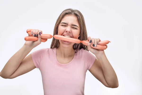Mujer joven sostiene conjunto de salchichas entre los dientes. Ella los sostiene con las manos. Aislado sobre fondo blanco . — Foto de Stock