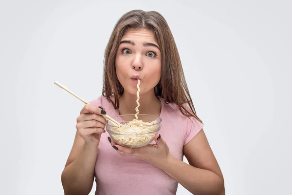 Uma jovem engraçada tem vermicelli na boca. Ela come-o com prazer. tigela modelo segurar com vermicelli na mão. Isolado sobre fundo branco . — Fotografia de Stock