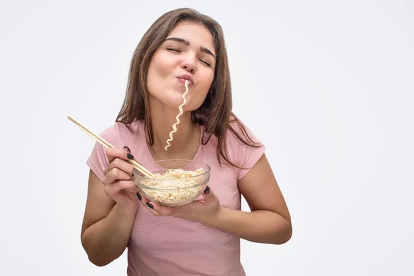 Vrolijke jonge vrouw eet vermicelli. Ze boog met het en vork in handen houden. Geïsoleerd op witte achtergrond. — Stockfoto