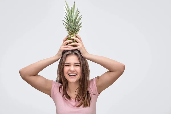 Θετική νεαρή γυναίκα χαμόγελο. Αυτή να κρατήσει pineappple στο κεφάλι με τα δύο χέρια. Απομονωμένα σε γκρι φόντο. — Φωτογραφία Αρχείου
