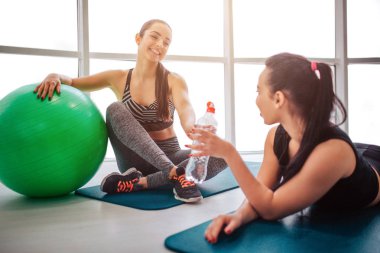 Oturma ve matrass üzerinde yalan iki genç arkadaşlar. Görüşmeler ve çalışmadan sonra dinlenin. Asya modeli su şişesi tutun. Avrupa kadın üzerinde yeşil fitball yalın.