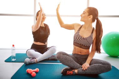 Mutlu genç kadın matrass üzerinde oturmak ve birbirlerine beşlik. Modelleri gülümse. Onlar-si olmak içinde yatsın fitness Oda aftr egzersiz.