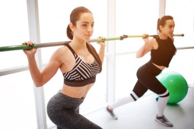 Ciddi genç kadınlar birlikte fitness salonunda egzersiz yoğunlaşmıştır. Onlar egzersiz zor. Omuzlarında halter modellerinde. Kadroları adım.