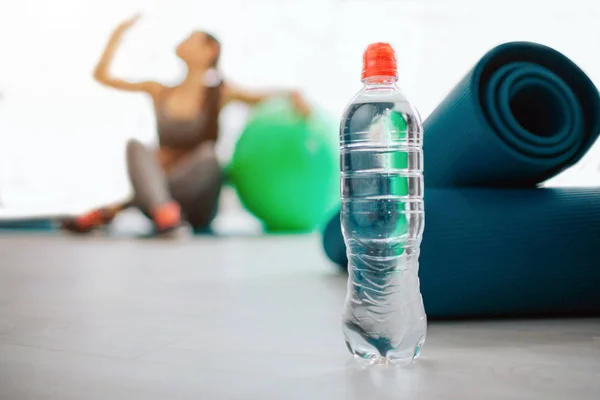 Wasserflaschen stehen beim Mann im Sportraum. junge Frau sitzt in der Nähe von Fitball und Waschbecken Wasser. sie befindet sich im hellen Zimmer haben Ruhe. — Stockfoto