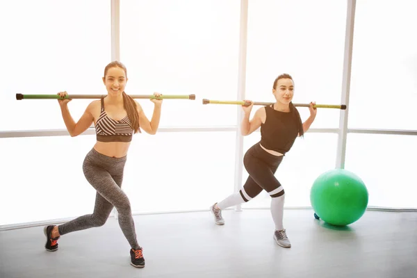 Giovani donne concentrate che si allenano in sala mensa. Tengono il bilanciere sulle spalle e fanno passi a fianco. Anche i modelli fanno mosse di squadra . — Foto Stock