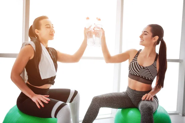 Mujeres jóvenes Haooy animando juntas. Se sientan en bolas verdes y se tocan botellas. Los modelos parecen felices . — Foto de Stock