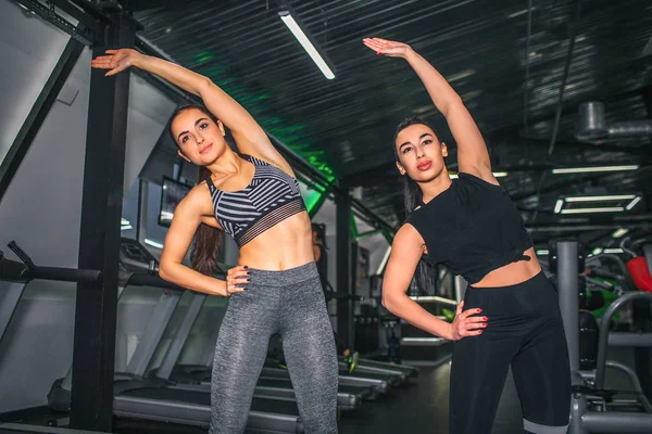 Mooi en vol vertrouwen jonge vrouwen die zich uitstrekt in de sportschool. Ze staan samen en mager aan kant. Modellen kijk uit en houden enerzijds op heupen. — Stockfoto