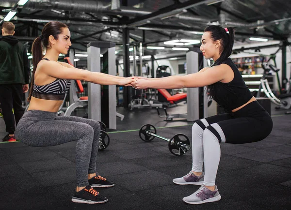 Giovani donne eccitate e felici si tengono per mano e in squadra. Guardano e sorridono. I modelli sono da soli in palestra . — Foto Stock