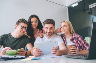 Güzel ve çekici genç insanlar birlikte masaya oturabiliriz. Tablet ve gülümseme bak. Esmer stnd arkalarında. Birlikte çalıştıklarını.