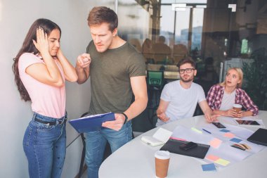 Kızgın genç amn plastik tablet woth kağıtları tutun ve üzerinde işaret edin. O kızgın ve çığlık. İki kişi onların arkasına otur. Bunlar hayret ve korkmuş. Esmer kulakları ve gözleri kapalı tutmak.