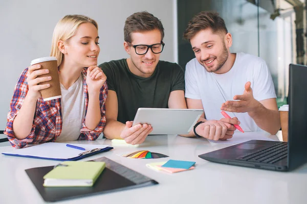Happy and cheerful young people work together at one table. Guy in black shirt hold tablet. They look at it all together. People are interested. — Stock Photo, Image