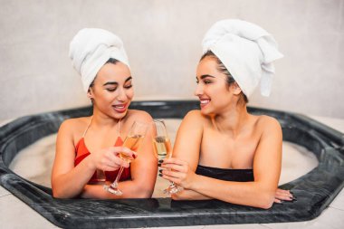 Neşeli ve mutlu eauropean ve Asyalı kadınlar birlikte jakuzide oturun. Bardak şampanya tutuyorlar. Modelleri gülümse. Onlar dinlen.