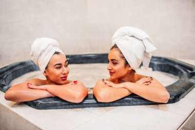 Güzel ve yakışıklı genç modelleri birbirlerine ve gülümseme bak. Jakuzide birlikte oturuyorlar. Saçlarını havlu ile sarılır. Genç kadın soğutma.