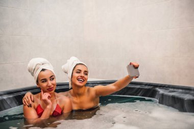 Mutlu genç kadını kabul selfie Asya arkadaşıyla beraber. Poz ve kameraya gülümse. Modelleri jakuzi ve birlikte oturup.