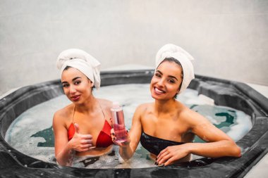 Neşeli ve çekici genç kadın Jakuzi ile köpük su dolu oturup. Avrupa modeli şişe duş jeli ile tutun. Asyalı kadın büyük başparmak yukarı kaldır. Onlar gülümseme.