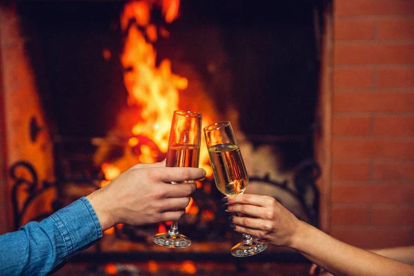 Vista cortada de manos de hombre y mujer sosteniendo vasos con champaña. Lo tocan frente a la chimenea. . — Foto de Stock