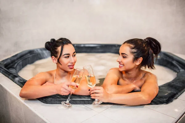 Alegre y sexy de las mujeres jóvenes tocando gafas. Se miran y sonríen. Los modelos se sientan en jacuzzi y refrigeración . —  Fotos de Stock