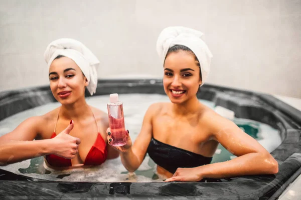 Photo de deux modèles assis dans un jacuzzi plein d'eau avec de la mousse. Gel douche European odel hold dans les mains. La femme ASIAN tient un gros pouce. Ils regardent droit sur la caméra . — Photo