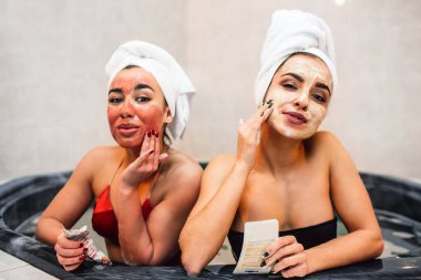 Güzel genç kadın Jakuzi kameraya bak. Beyaz ve kırmızı maske yüzlerinde koydular. Modelleri suya otur. Onlar rahatlatıcı ve tüyler ürpertici.