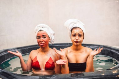 Üzgün ve mutsuz genç kadın kameraya bak. Yüzünde bazı güzellik maskesi koymak. Modelleri bir kenara vücut elele tutuşun. Jakuzi içinde oturuyorlar.