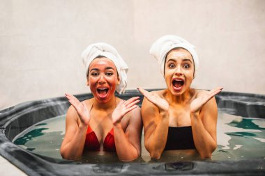 Çok mutlu genç kadın Jakuzi su dolu oturup ve kameraya bak. Onlar hayret ve hayrandı. Güzellik maskeleri modelleri var.