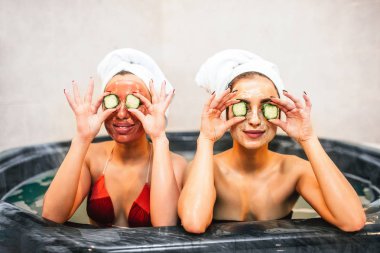 Komik genç kadın jakuzide oturun ve salatalık parçaları gözünü tutun. Onlar güzellik yordamlar ve spa odasında olduğunu. Modelleri mutlu görünüyorsun.